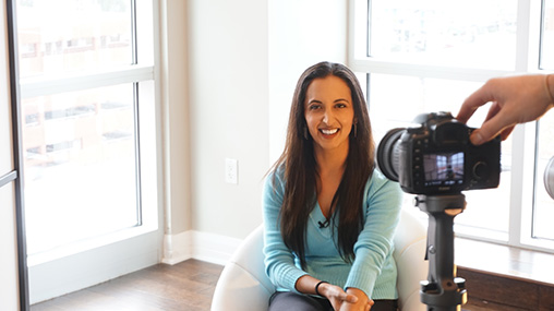 paula_home_tv_2 Paula Pant being filmed for the 'Your First Rental Property' course, smiling while seated in a bright, modern space with a camera visible in the frame, representing the professional educational content offered through Afford Anything.
